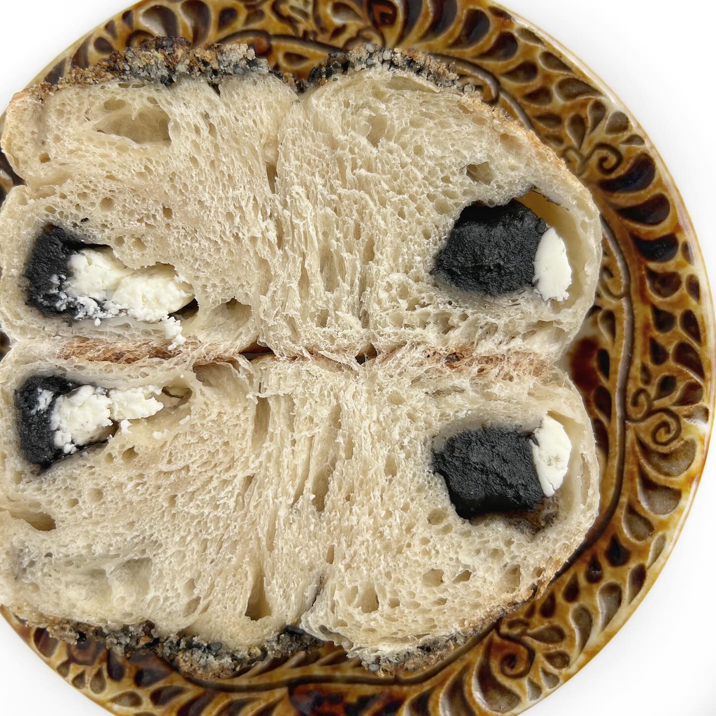 AZU BAGELさんのベーグル「黒ごまあんクリームチーズ岩塩黒ごまクランブルトッピング」を横に切った断面写真。黒ごまあんとクリームチーズが入っています。