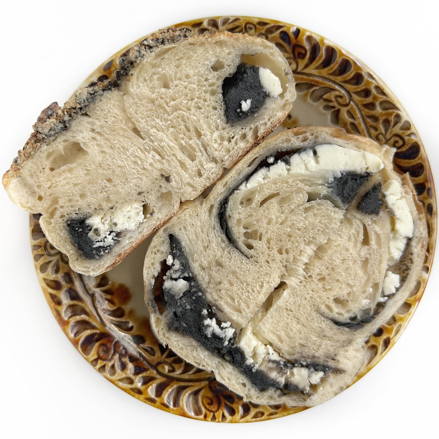 AZU BAGELさんのベーグル「黒ごまあんクリームチーズ岩塩黒ごまクランブルトッピング」を縦に切った断面写真。