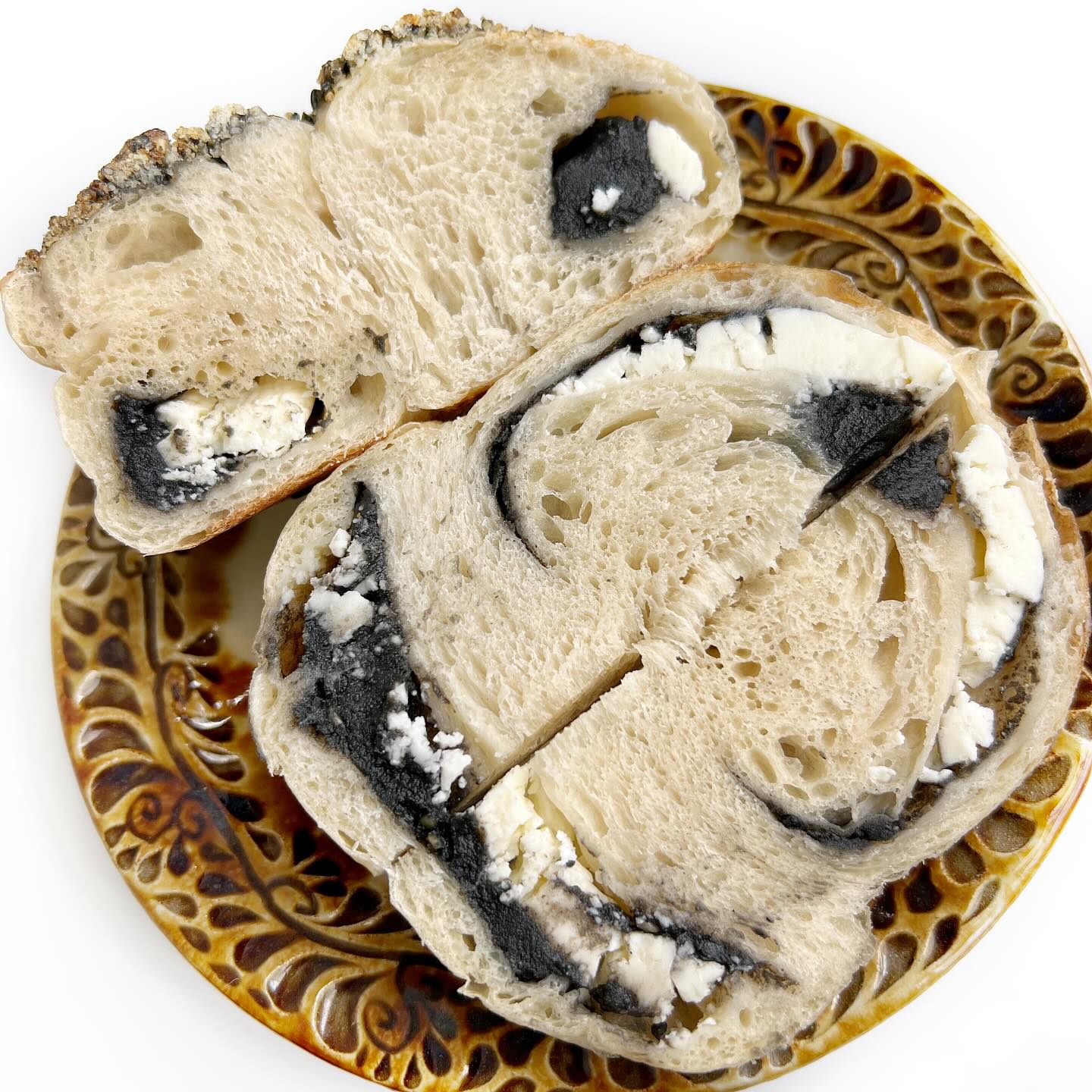 AZU BAGELさんのベーグル「黒ごまあんクリームチーズ岩塩黒ごまクランブルトッピング」を縦に切った断面写真。黒ごまあんとクリームチーズがたくさん入っています。