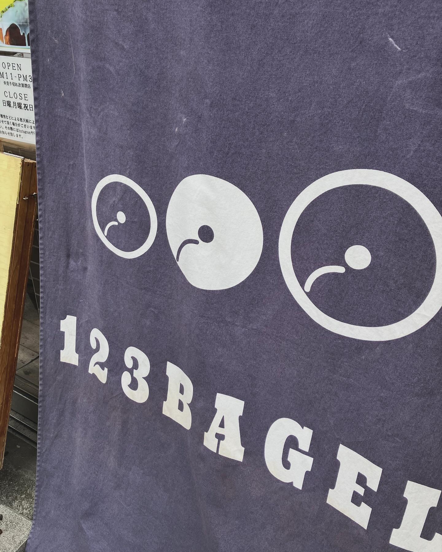 日本の東京都中央区日本橋小伝馬町にあるひふみベーグルさんの店頭ののれん。紺色の布地に白で123BAGELと書かれている。