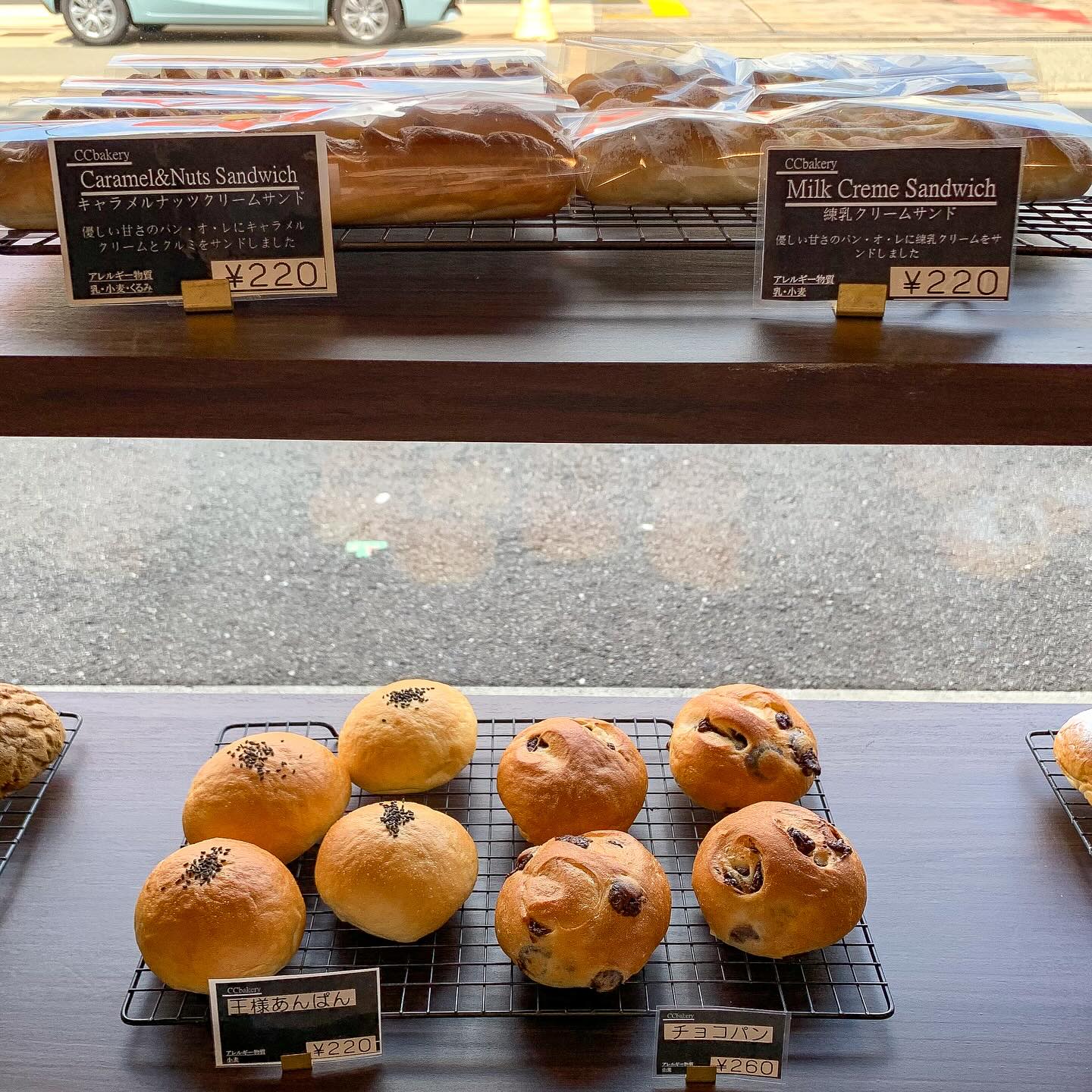 日本の大阪・西天満にあるCC Bakeryの店内写真。
棚の上段にキャラメルナッツクリームサンドと練乳クリームサンドが、下段に王様アンパントチョコパンが写っている。