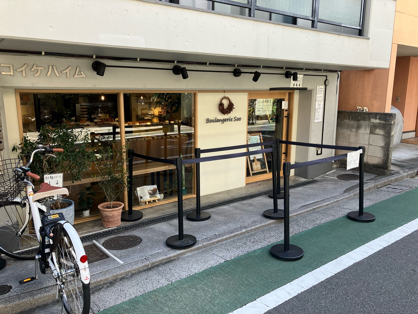 日本の志村坂上のベーカリー ブーランジェリースーの店舗外観。コンクリートと木枠、黒の手すり、道路のグレーと緑色と白線が洗練された印象。
