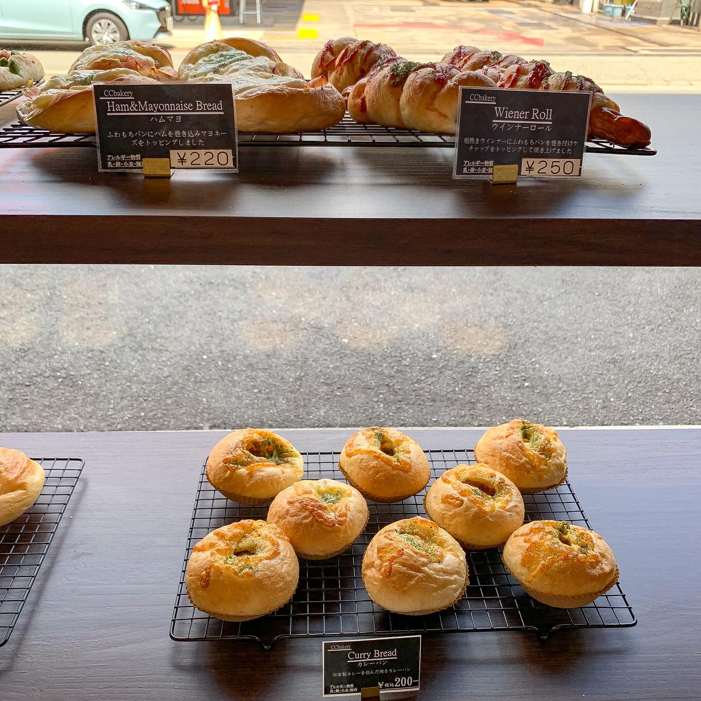日本の大阪・西天満にあるCC Bakeryの店内写真。
棚の上段にハムマヨとウインナーロールの総菜パンが、下段にカレーパンが写っている。